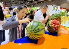 Carving artist is carving with watermelons at the Joy Wing Mau stand. /雕刻师在佳沃鑫荣懋摊位上雕刻西瓜。 