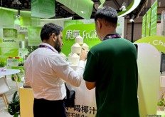 A representative from Guoke (right) is demonstrating the coconut opener to a visitor (left). / 果氪的代表（右）正在向参观者（左）演示椰子开瓶器。 