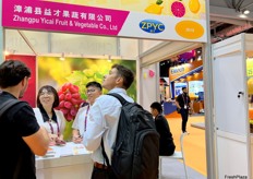 A representative of Zhangpu Yicai Fruit and vegetables (second left) is talking with visitors at their stand. / 漳浦益才果蔬代表（左二）在展位与参观者交谈。